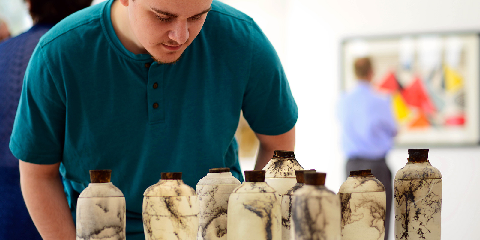 A man leans over to look at small artistic bottles.