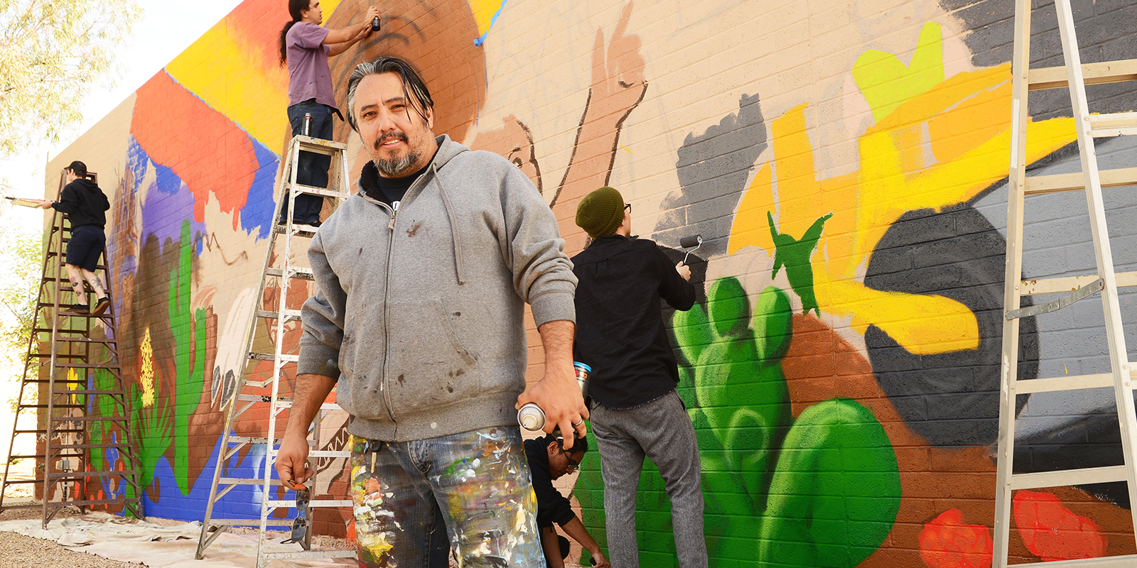 Four artists spray painting a mural on a brick wall.