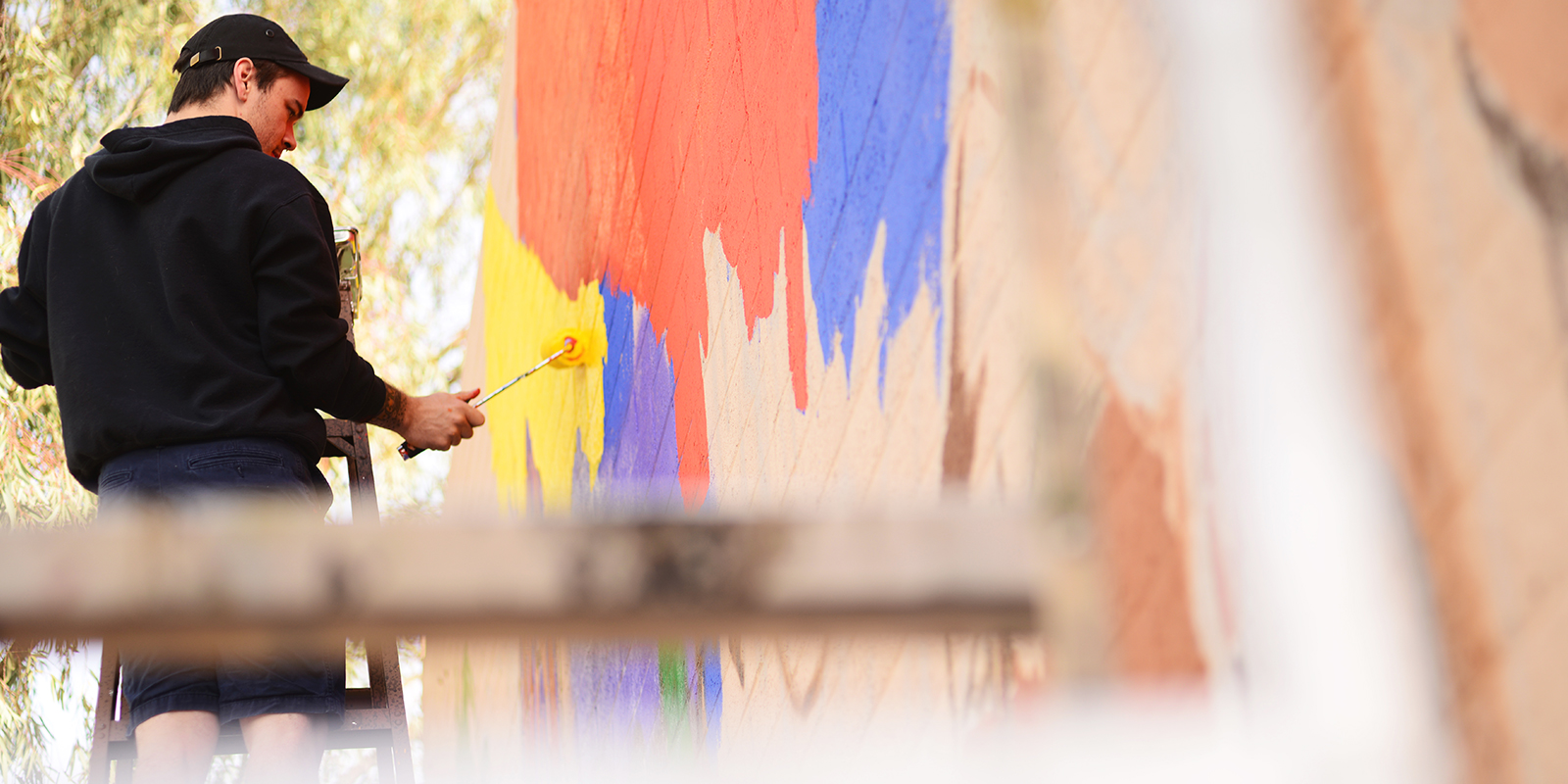 A man on a ladder uses a rolling paint brush.