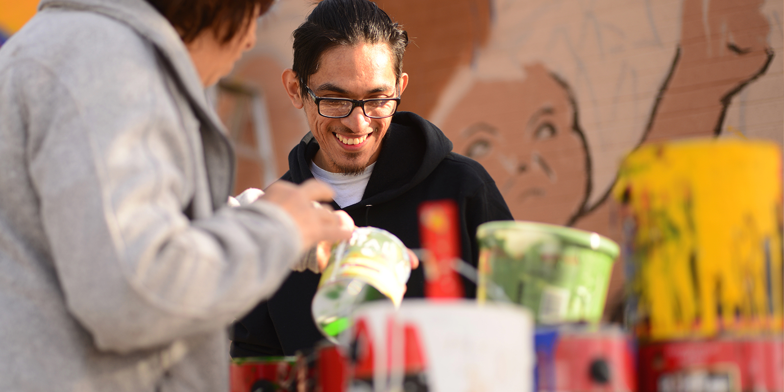 A man smiling and looking at cans of paint.