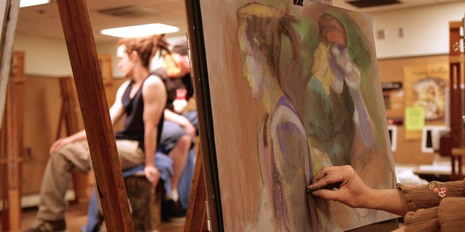 Hands drawing a portrait as two men pose.