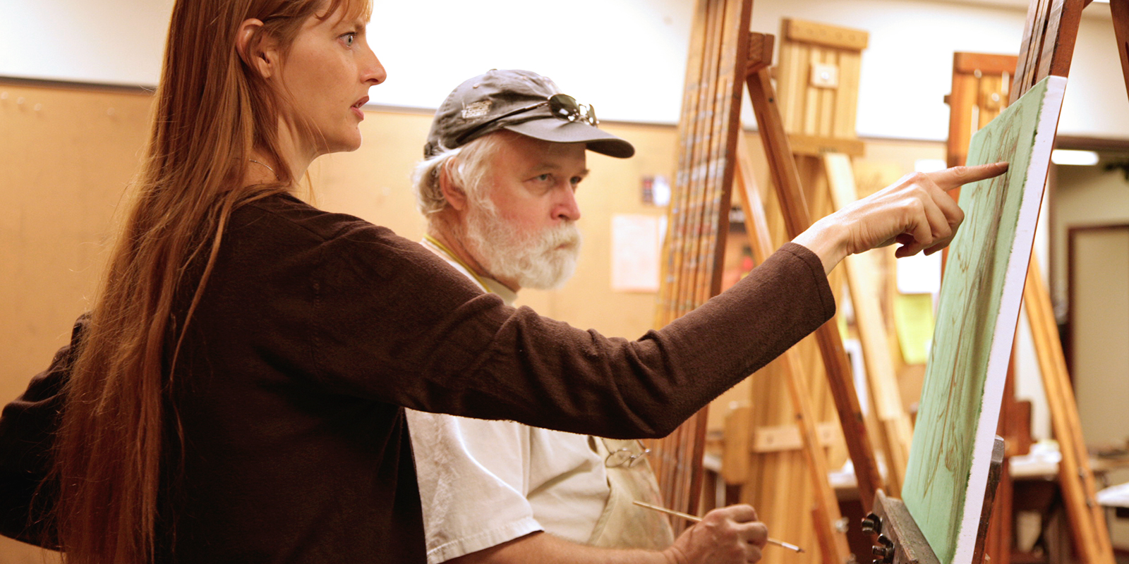 Instructor and student discuss a canvas on easel.