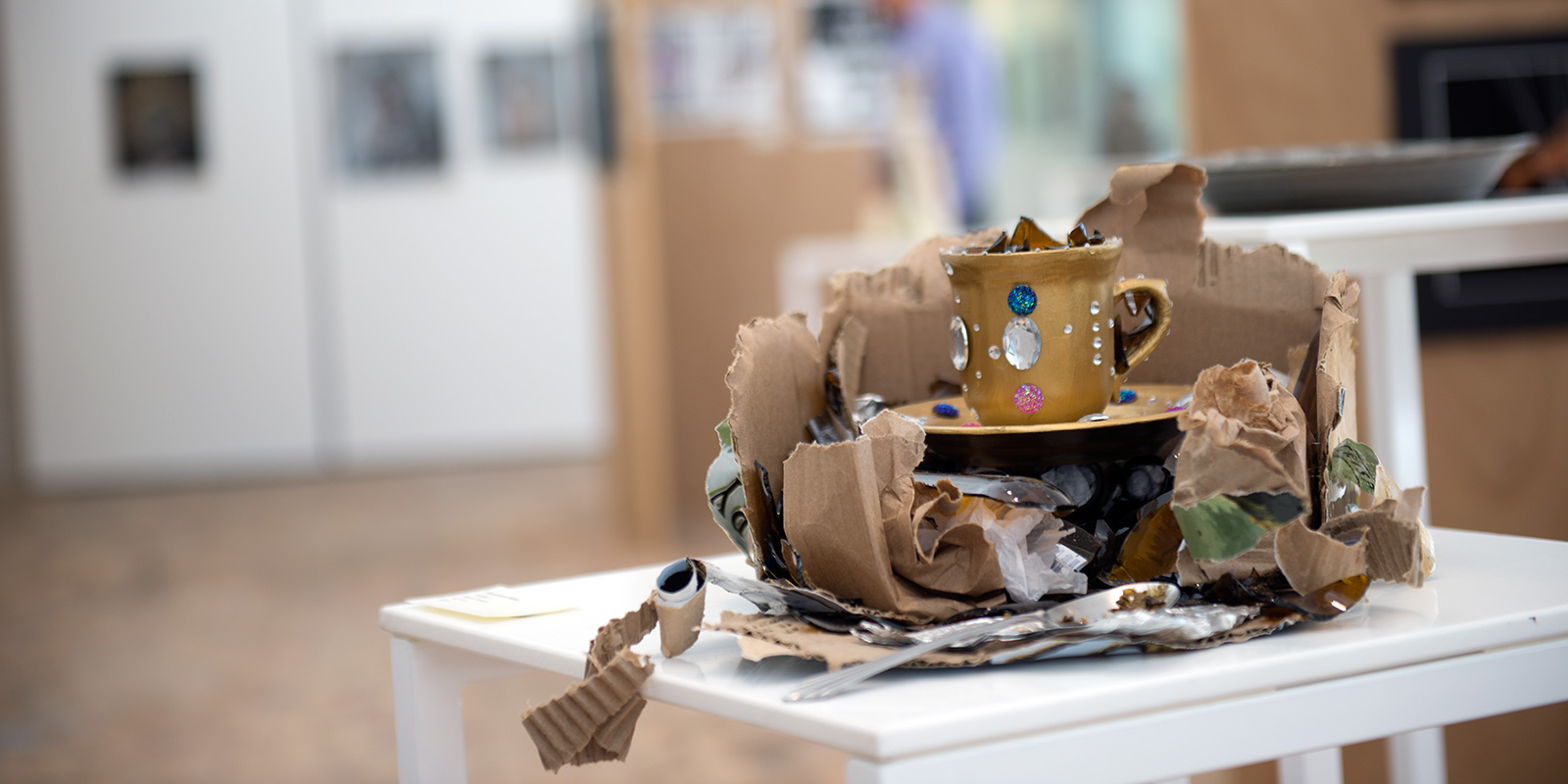 Art display with a coffee cup rest on a bed of cardboard.