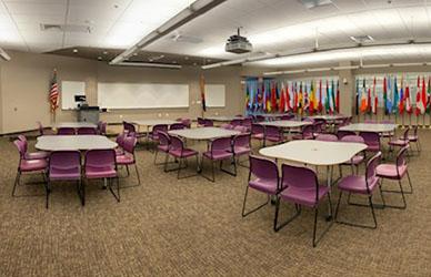 A grouping of tables and chairs in a large room with flags in the background