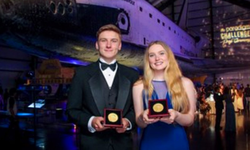 Two students hold up medals with a space shuttle behind.