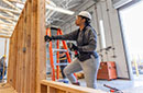 A person wearing a hard hat working on a wood wall frame