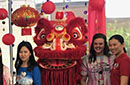 Three people stand in front of a Chinese dragon and paper lanterns