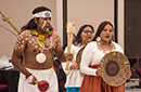 Three Indigenous people in traditional attire and body paint on campus