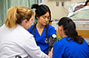 Three students in medical scrubs, one with a blood pressure cuff on