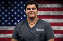 MCC graduate Gabe Gamboa wearing scrubs in front an American flag background