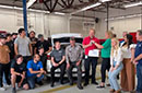 A group of people posing with two sitting in the trunk of an electric car