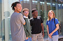 Four smiling students in a semicircle outside on the MCC campus