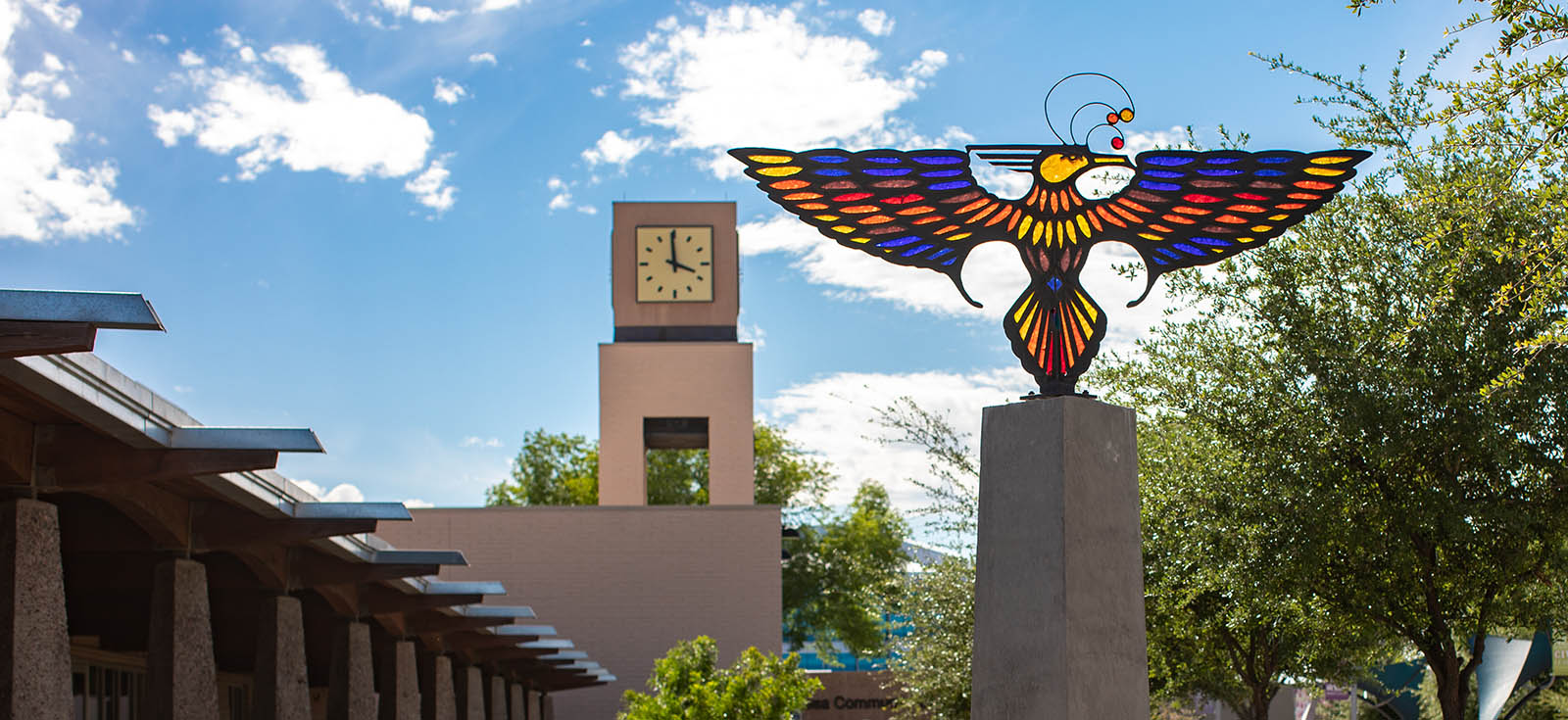 A stained glass Thunderbird statue with the MCC clock tower in the background