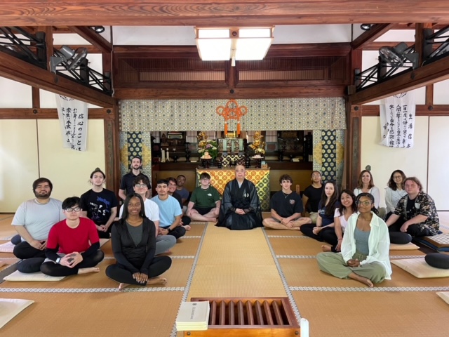 A group of students indoors sitting with legs crossed