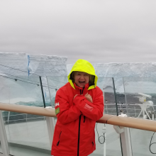 Woman in red jacket with yellow hat on a cruise ship near ice