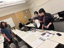 Four students standing and looking at documents on a classroom table