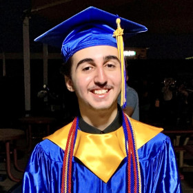 Smiling male teenager in blue graduation cap and gown.
